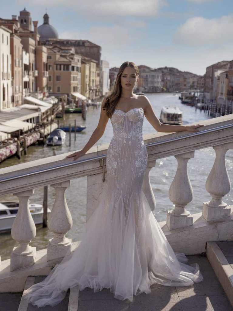 In questa foto una modella indossa un abito da sposa semisirena di Ricca Sposa 2023