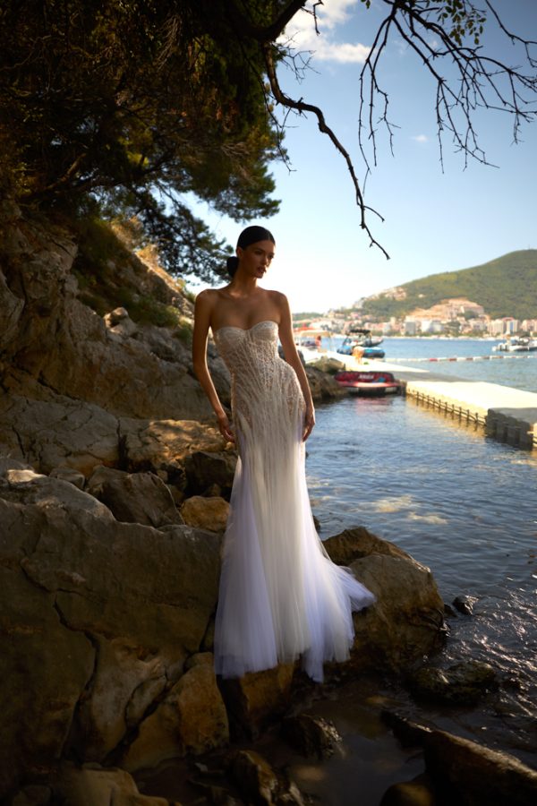 In questa foto, una modella su uno scoglio mentre indossa un vestito da sposa sirena 2023