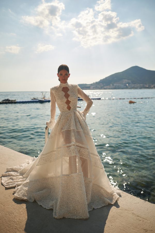 In questa foto una modella, mentre posa su un molo, indossa un abito da sposa dalla linea ad A in pizzo all over