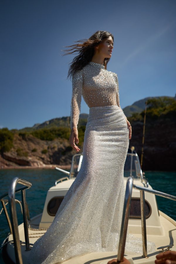In questa foto una modella, su una barca, indossa un abito da sposa con dettagli gioiello all over