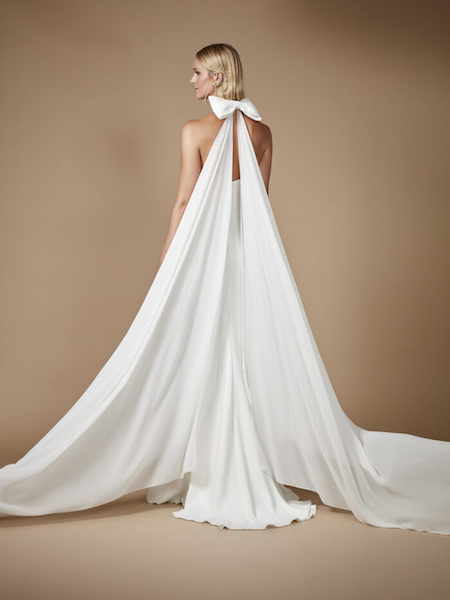 In questa foto una modella di spalle mostra il fiocco che chiude lo scollo all'americana del vestito da sposa e diventa il punto di apertura di due straordinarie ali di tessuto