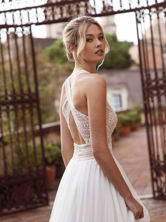 In questa foto una modella di spalle, mentre indossa un abito da sposa con schiena semi-scoperta: è incorniciata da due lembi di tessuto che si intrecciano