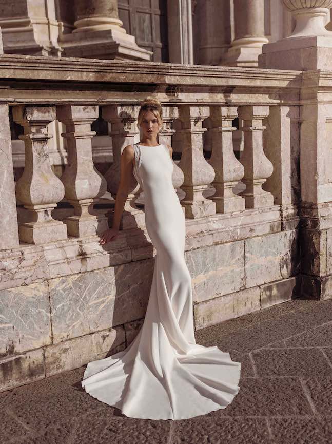 In questa foto una modella posa indossando un abito da sposa dalla linea a sirena della collezione Revelation di Modeca 2023