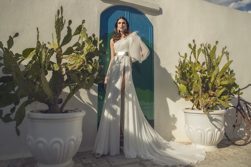 In questa foto una modella posa con un abito da sposa monospalla in chiffon, con manica balloon e sulla spalla un'applicazione plumage. Il vestito è della collezione Ellenica, di Pietro Demita Haute Couture 2023