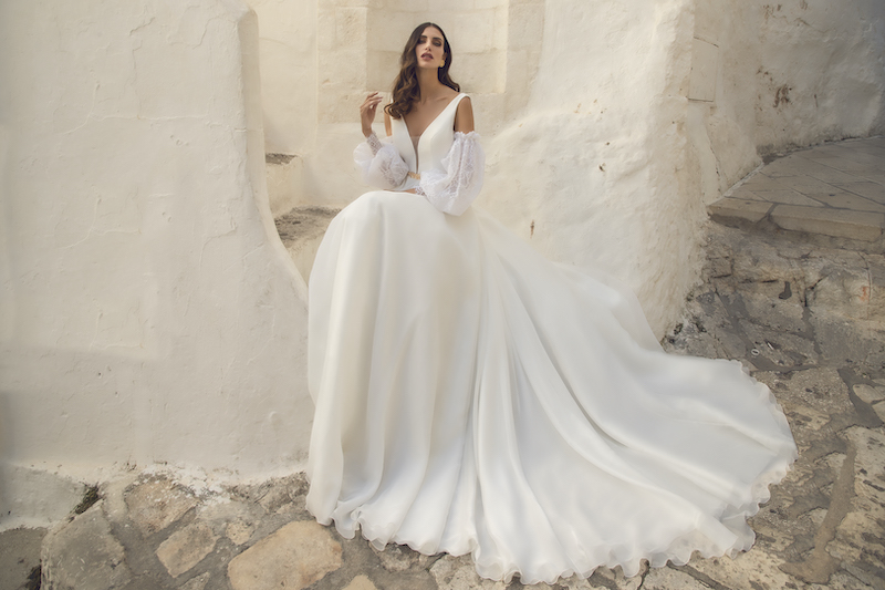 In questa foto una modella indossa un abito da sposa in mikado con scollo a V e maniche staccabili balloon. Sulla vita, un cinturino dorato