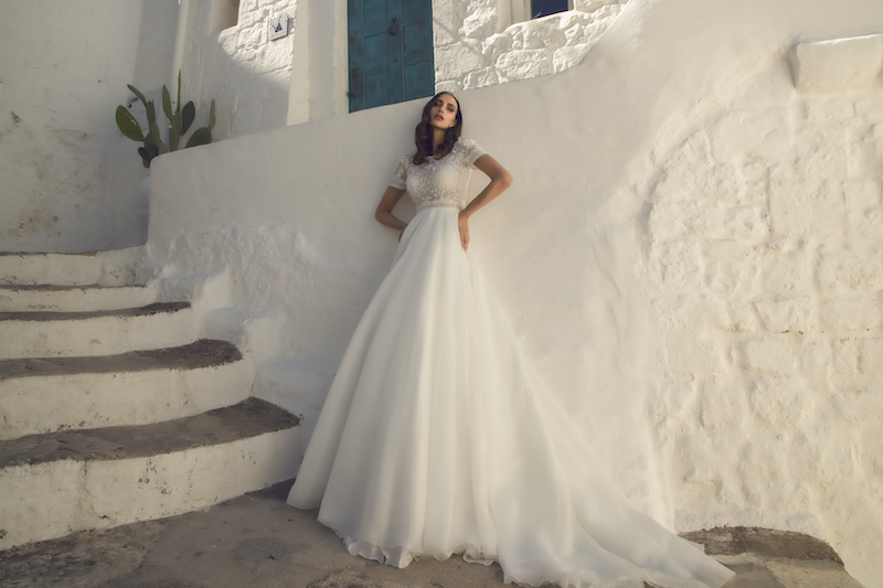 In questa foto una modella indossa un abito da sposa Pietro Demita Haute Couture 2023: il top è in pizzo con manichette corte, la gonna in organza di seta