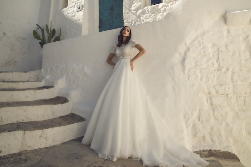 In questa foto una modella indossa un abito da sposa Pietro Demita Haute Couture 2023: il top è in pizzo con manichette corte, la gonna in organza di seta