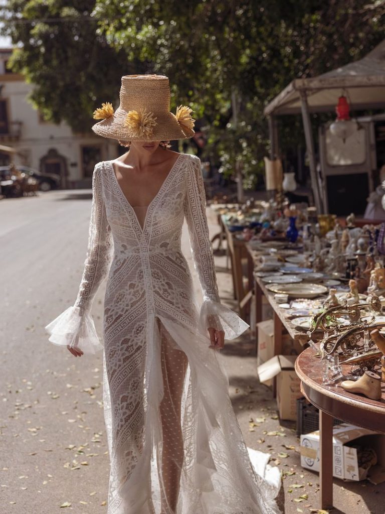 In questa foto una modella passeggia tra i viali di un mercatino di Palermo indossando un abito da sposa Boho Chic 2023. Fa parte della collezione Pinella Passaro