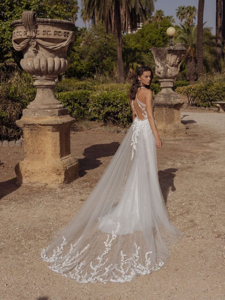 In questa foto una modella di spalle mostra la scollatura sulla schiena dell'abito da sposa. Il vestito di Pinella Passaro ha un sopragonna rimovibile