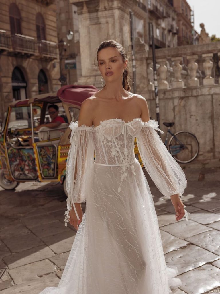 In questa foto una modella indossa un abito da sposa con corpetto con coppe e stecche in vista e maniche balloon staccabili. Il vestito è della collezione Pinella Passaro 2023