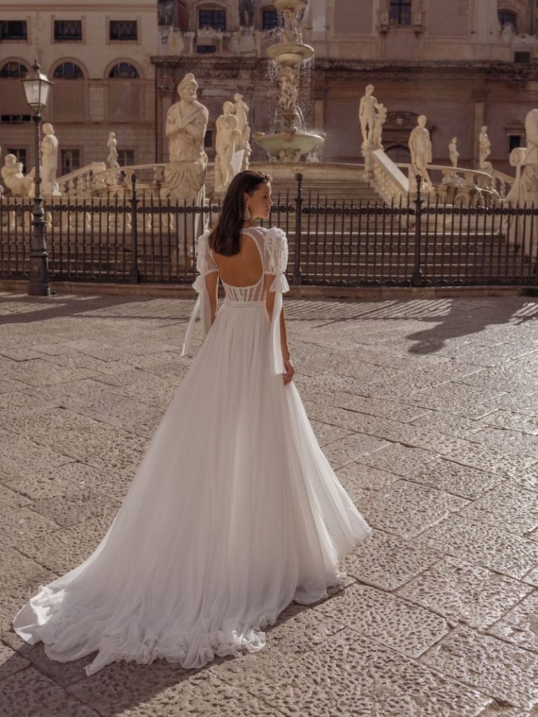 In questa foto una modella di spalle mostra la scollatura a goccia dell'abito da sposa di Pinella Passaro 2023