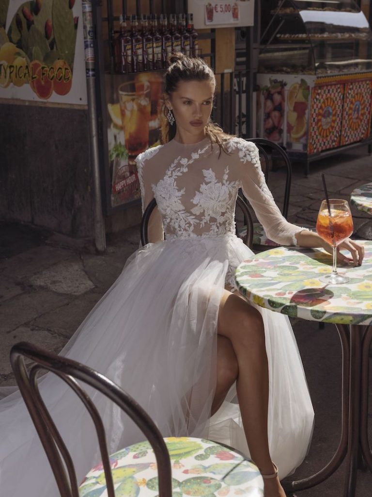 In questa foto una modella seduta mentre indossa un abito da sposa con top in tulle mano seta e ricami di pizzo in forma di ramage floreale