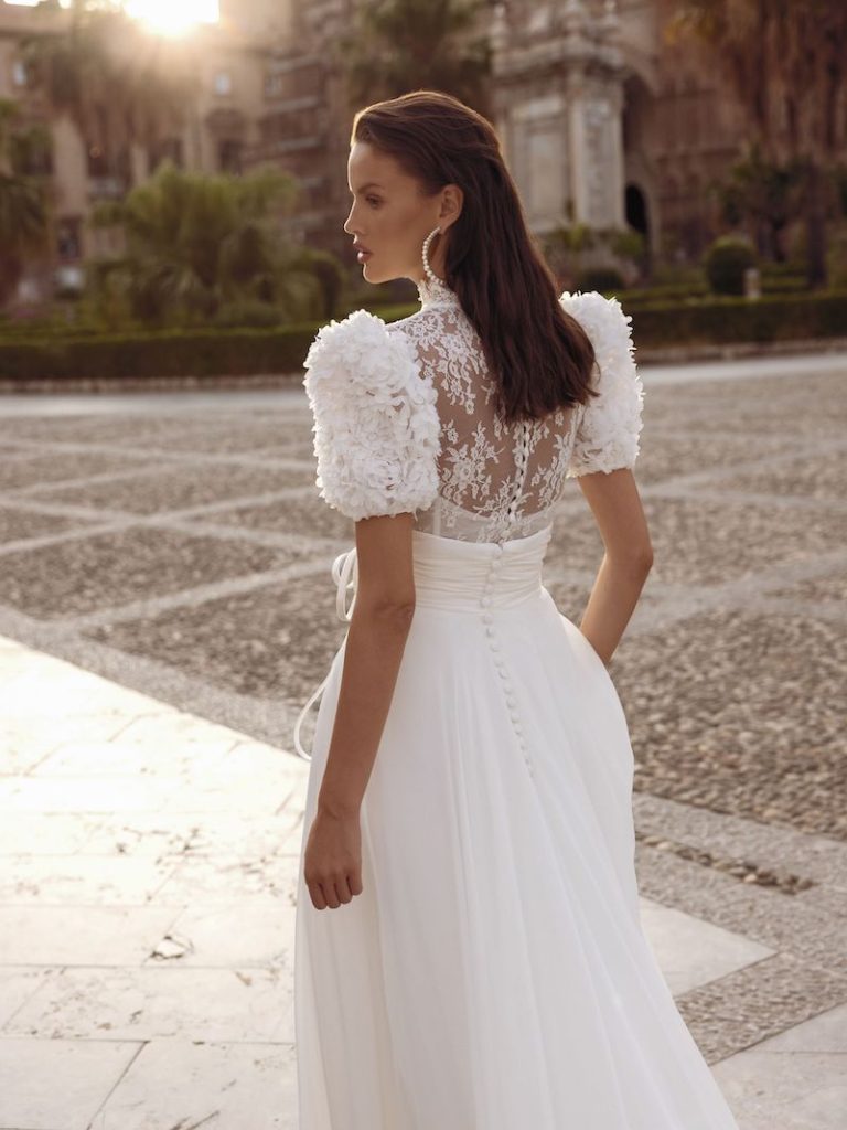 In questa foto una modella indossa un leggero e romantico abito da sposa con maniche corte a palloncino, impreziosito dall'applicazione di piccole ruches in tessuto