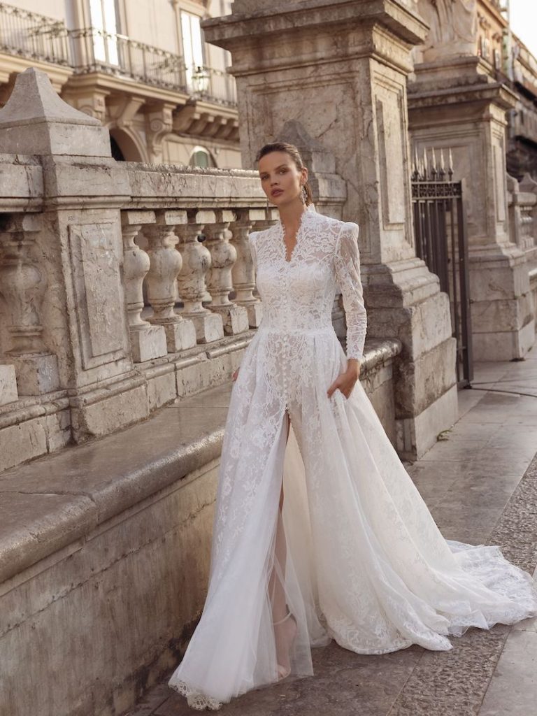 In questa foto una modella passeggia indossando un abito da sposa in pizzo all over di Pinella Passaro. Splendido lo scollo Queen Anne