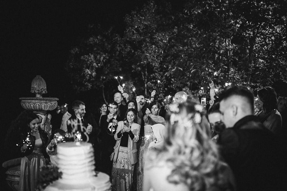 In questa foto in bianco e nero il taglio torna di un matrimonio realizzato dal fotografo Fabrizio Musolino: gli sposi di spalle festeggiano insieme ai loro invitati