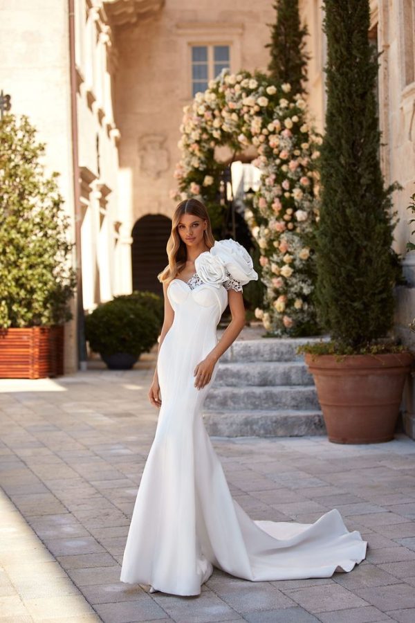 In questa immagine un abito da sposa a sirena Milla Nova 2023 con maxi fiori sulla spalla.