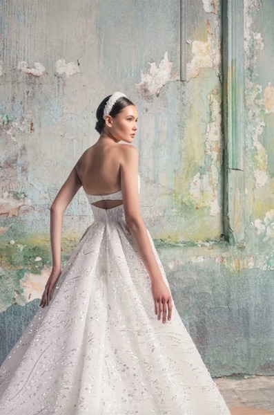 In questa foto una modella di spalle indossa un abito da sposa bianco con applicazioni di cristalli e dettagli lurex