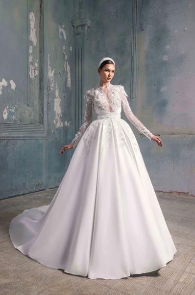In questa foto una modella indossa un importante abito da sposa in mikado di seta. Il vestito ha le maniche lunghe e la parte alta è totalmente lavorata in pizzo con applicazioni 3D