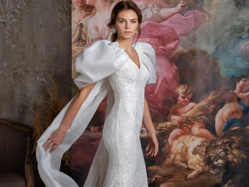 In questa foto una modella posa con uno degli abiti da sposa Papilio 2023 a sirena con maniche balloon e lungo strascico in chiffon
