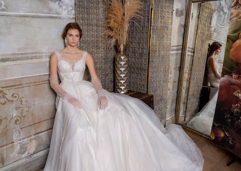 In questa foto una modella posa seduta indossando un abito da sposa ampio in tulle con guanti lunghi abbinati