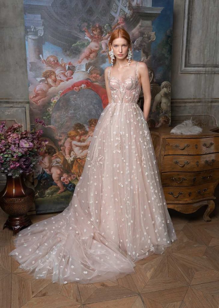In questa foto una modella indossa un abito da sposa Papilio 2023 in tulle di colore rosa pesca con micro fiori sia su corpetto che sulla gonna. La modella indossa maxi orecchini ricamati abbinato 
