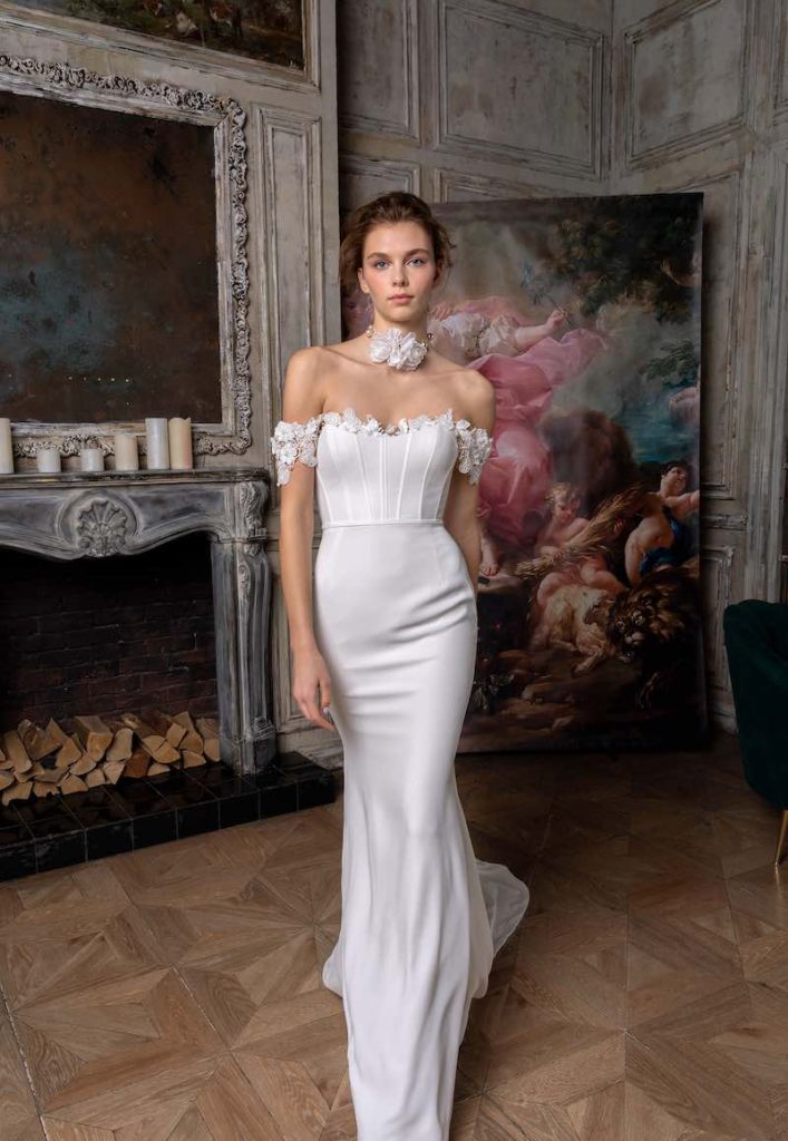 In questa foto una modella indossa un abito da sposa a sirena Papilio 2023 con bustier con bordo di fiori e choker abbinato 