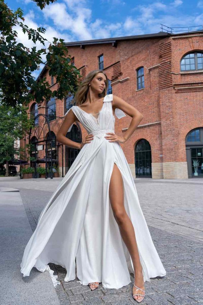 In questa foto una modella indossa un abito da sposa Papilio 2023 scivolato con spacco laterale, scollo a V e fiocchi sulle spalle 