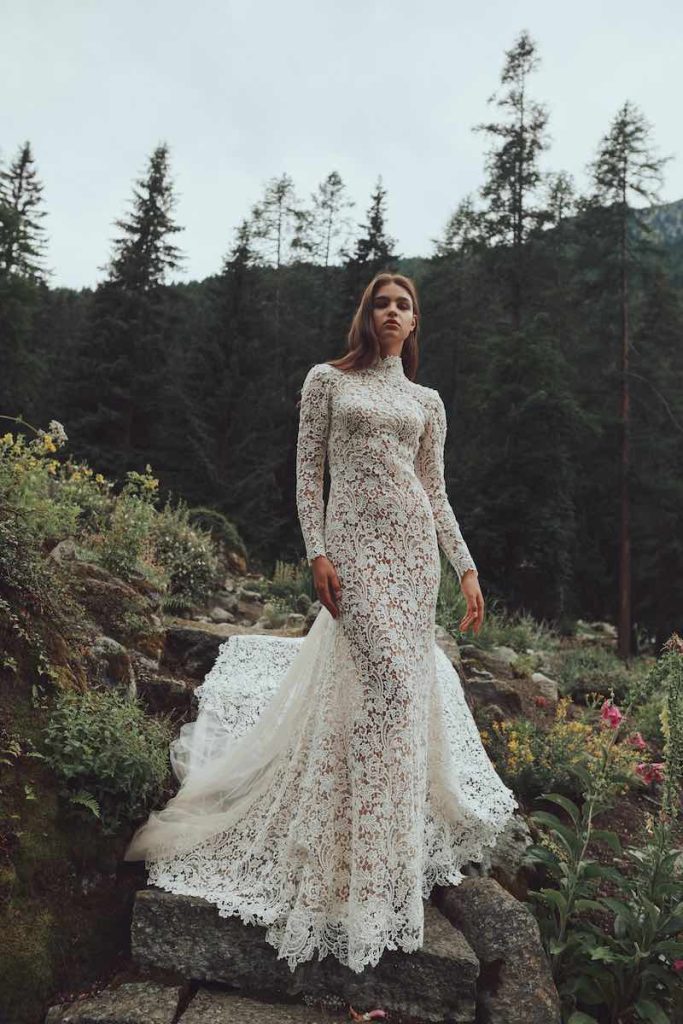 In questa foto una modella indossa un abito a sirena Alessandro Angelozzi Couture 2023 con lunga coda, collo alto e maniche lunghe interamente in pizzo macramè