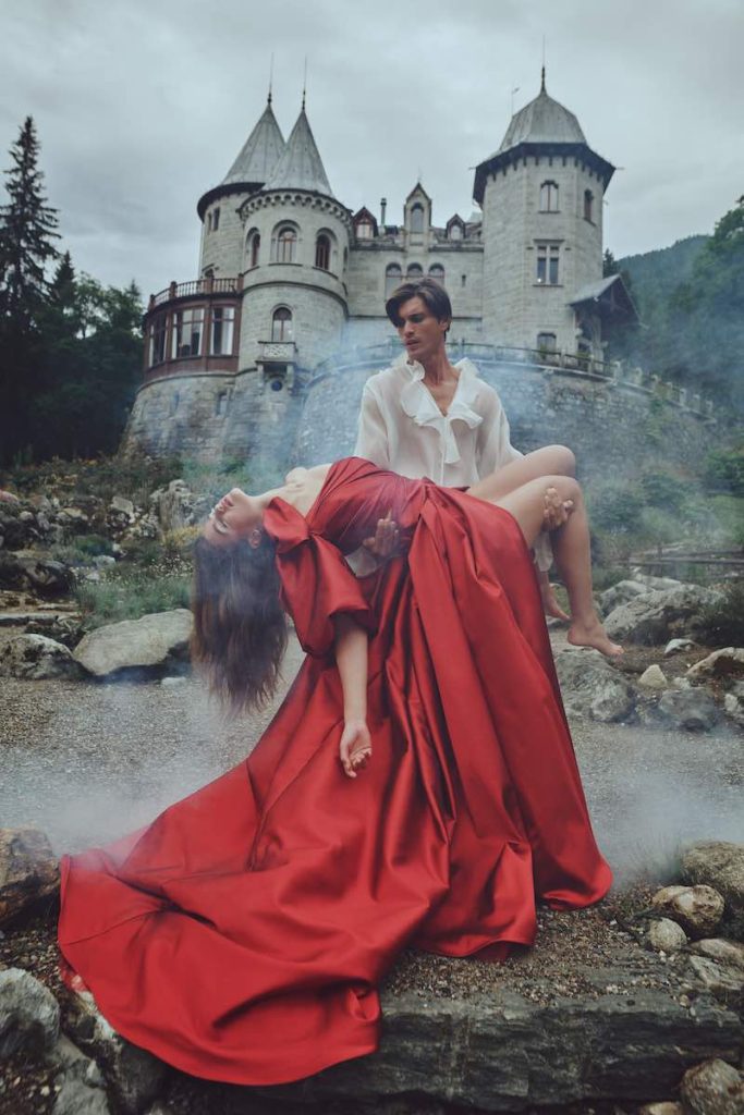 In questa foto una modella posa in braccio ad un modello indossa un abito da sposa ampio in mikado di seta di colore rosso carminio e con maniche balloon lunghe fino al gomito