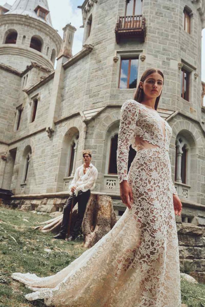 In questa foto una modella indossa un abito da sposa a mezza sirena con leggera coda Alessandro Angelozzi Couture 2023 in guipure con dettaglio cut out sui fianchi e maniche lunghe