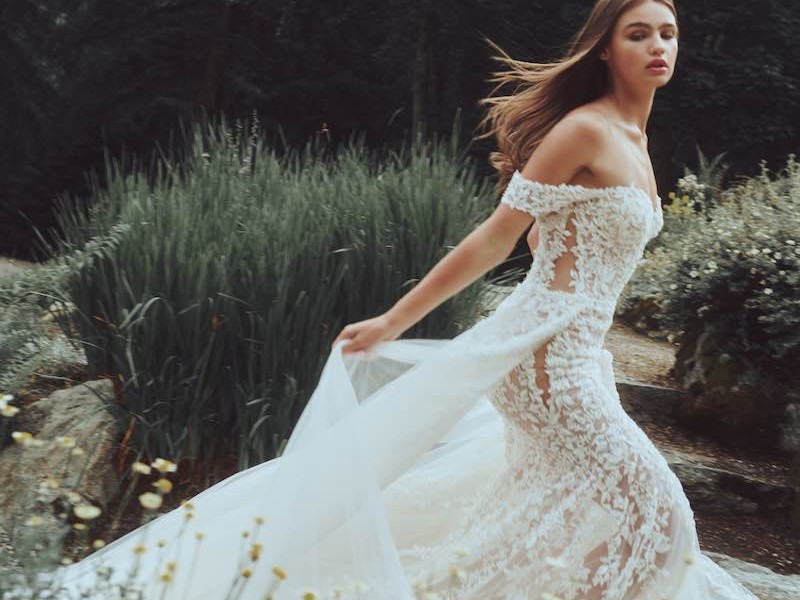 In questa foto una modella corre indossando un abito di Alessandro Angelozzi Couture 2023 in pizzo con sopragonna in tulle e maniche off shoulder