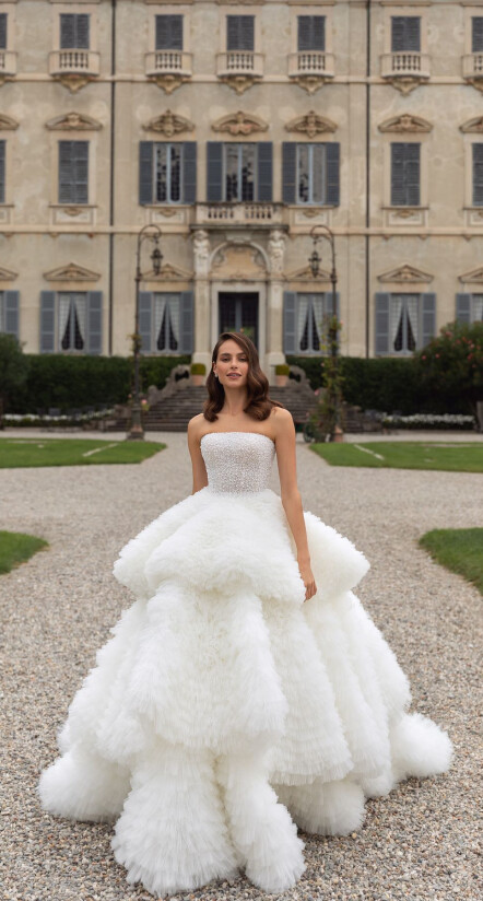In questa foto una modella, passeggiando nel giardino di una villa sul Lago di Como, indossa un vestito con gonna a maxi balze. L'effetto voluto dal brand Pollardi è quello di una nuvola