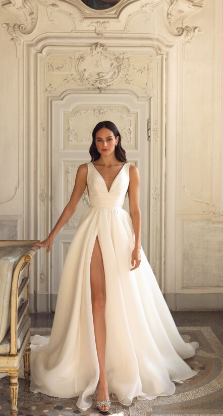 In questa foto una modella indossa un abito da sposa dalla linea ad A, con scollo a V e spacco. Il vestito, di Pollardi, è semplice e dalle linee essenziali