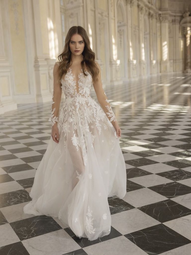 In questa foto la modella indossa un abito da sposa scivolato con fiori tridimensionali Capri Sposa 