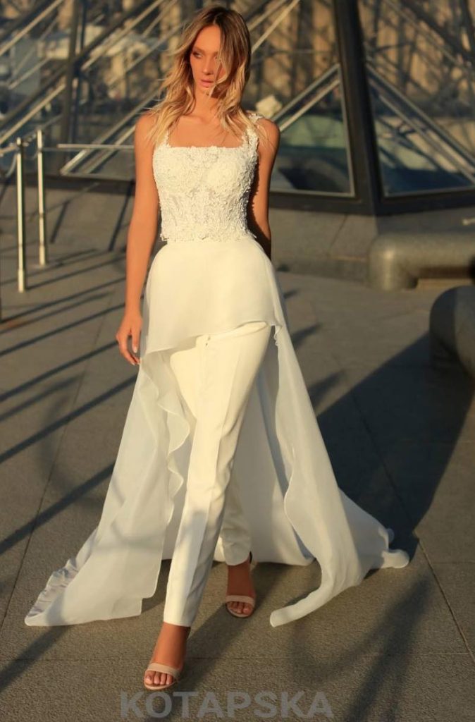 In questa foto una modella fotografa davanti alla Piramide del Louvre indossa un abito da sposa trasformabile di Iryna Kotapska con pantaloni, bustier in pizzo con scollo quadrato e sopragonna in chiffon 