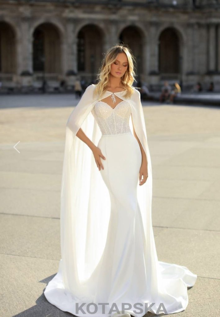In questa foto una modella indossa un abito da sposa a sirena con bustier in pizzo, gonna in chiffon e mantella abbinata legata al collo