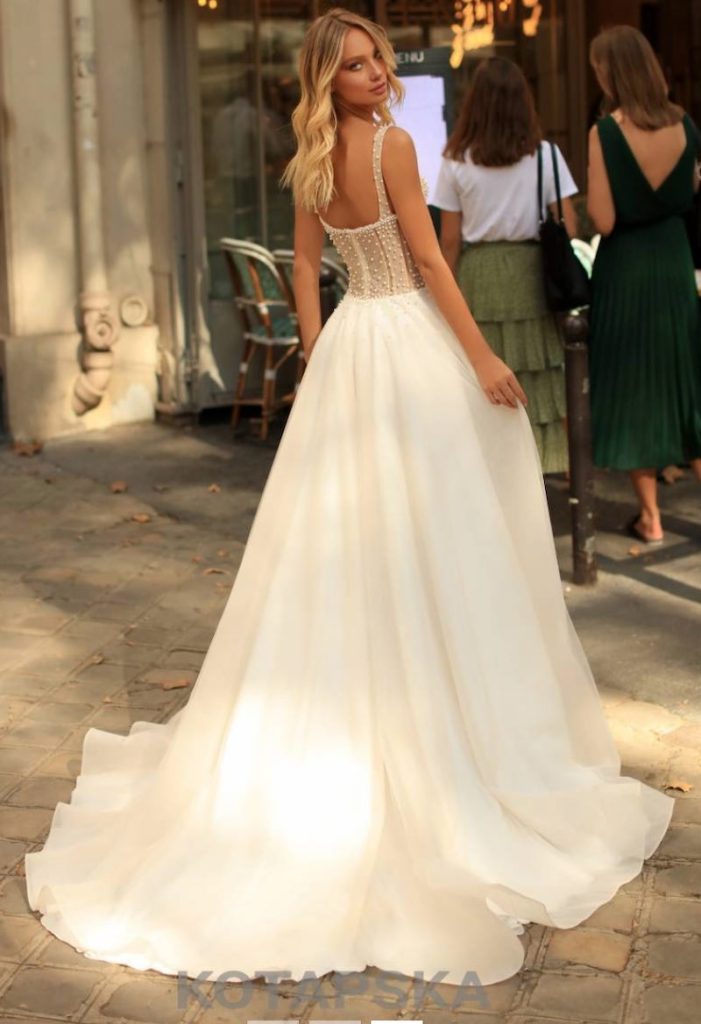 In questa foto una modella ritratta di spalle per strada indossa un abito da sposa ad A con gonna ampia in chiffon e corpetto ricamato con perline