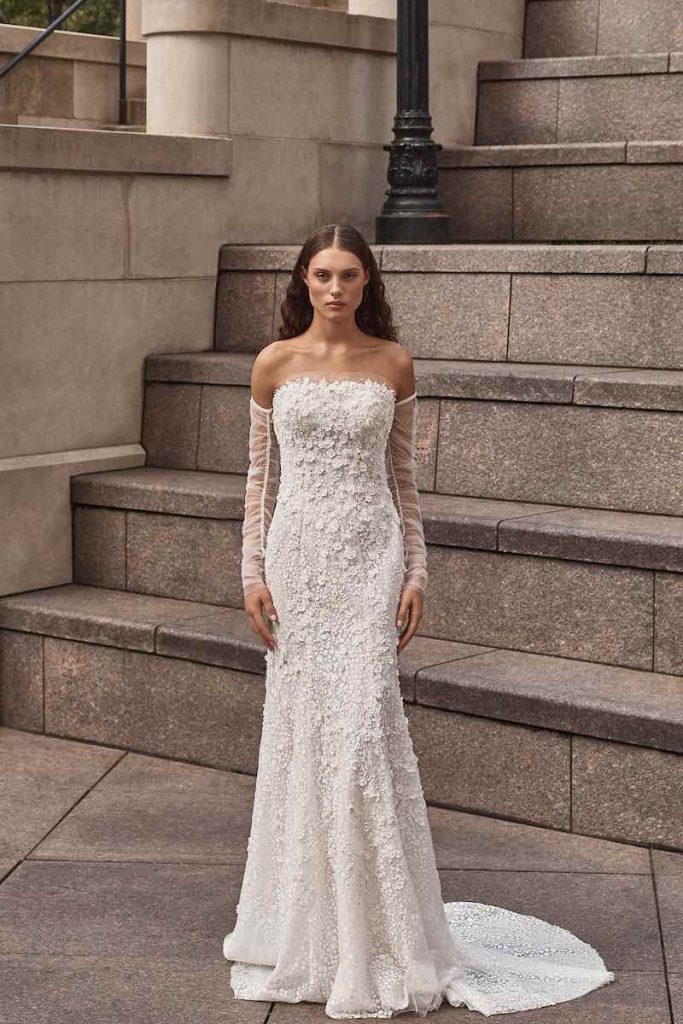 In questa foto una modella indossa un abito da sposa un abito da sposa La Premiere Bridal 2023 a mezza sirena con ricami floreali 3D e maniche a guanto rimovibili in tulle
