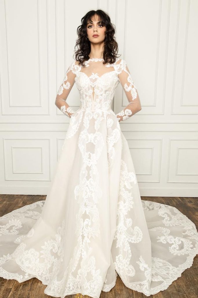 In questa foto una modella indossa un abito da sposa dalla linea ad A in tulle ricamato con maniche lunghe effetto tattoo e scollatura illusion