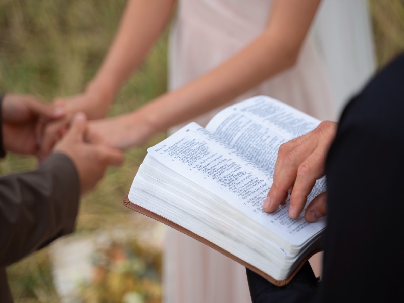 In questa foto il dettaglio di un sacerdote con il libretto messa matrimonio aperto davanti a due sposi che si tengono per mano