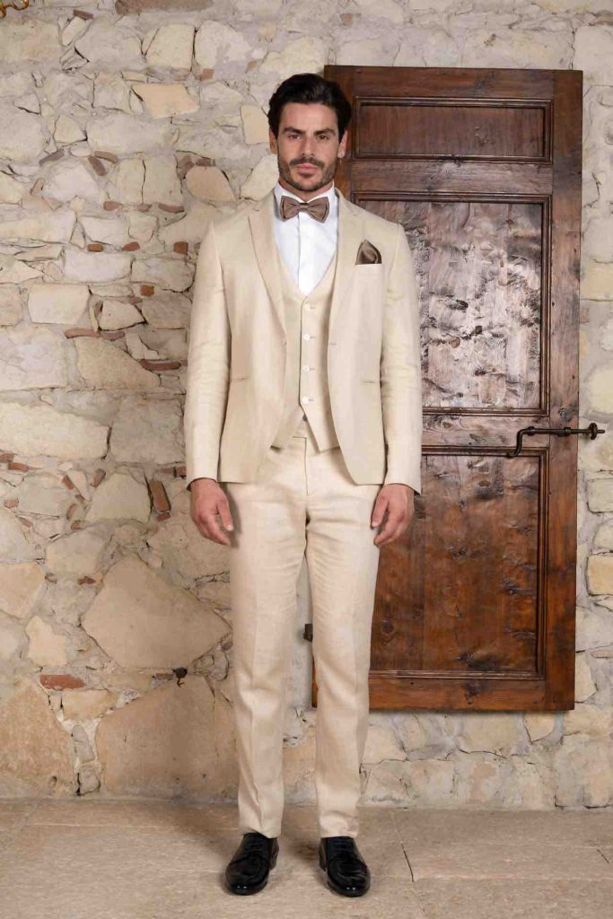In questa foto il modello e attore Andrea Casalino indossa un abito di lino color sabbia, con papillon e pochette marroni