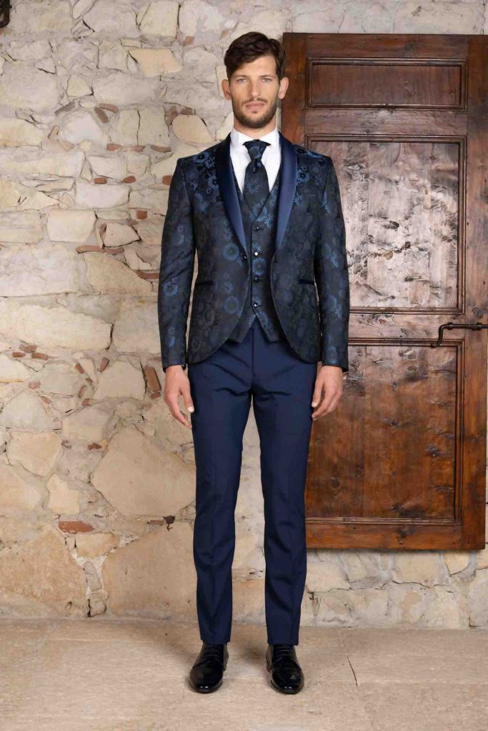 In questa foto il modello indossa un vestito blu la cui particolarità sta nel pattern damascato che rivitalizza giacca, gilet e plastron