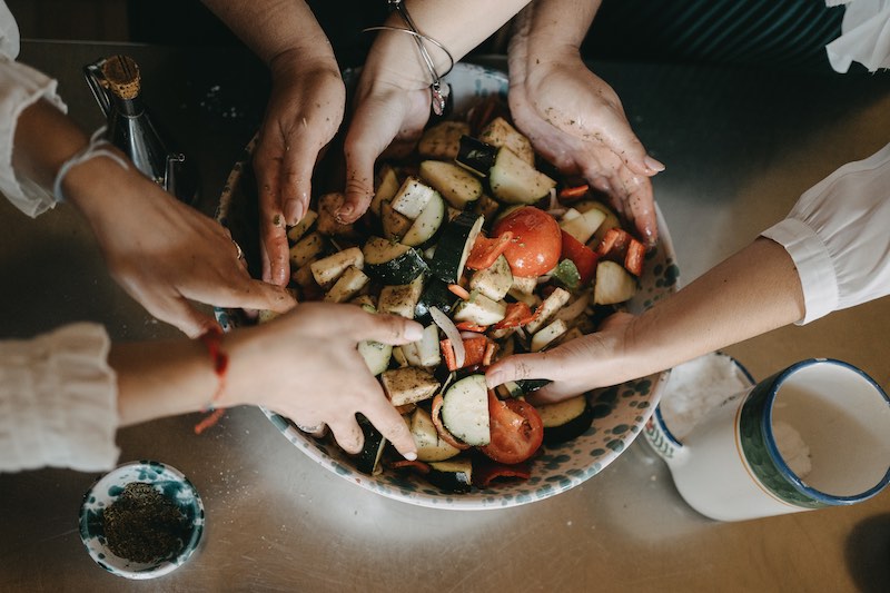 In questa foto il dettaglio di mani che mescolano un insalata di verdure fresche