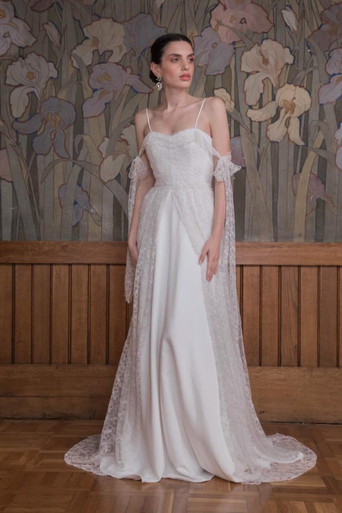 In questa foto una modella indossa un abito da sposa More 2023 in cady di seta con sopra uno strato di garza ricamata. La stessa organza è usata per fiocchi che scendono morbidi sulle braccia