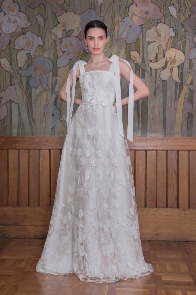 In questa foto una modella indossa un abito della collezione sposa 2023 More in tulle ricamato con motivi floreali e fiocchi di velluto sulle spalle