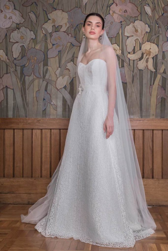 In questa foto una modella indossa un abito da sposa componibile in pizzo Chantilly con gonna ampia e scollo a cuore. la modella indossa anche un velo in tulle