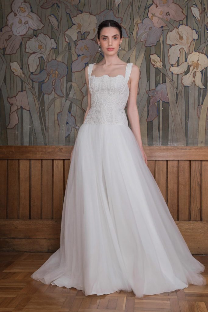 In questa foto una modella indossa un abito da sposa More 2023 con gonna in tulle e corpetto in pizzo macramè con bretelline larghe