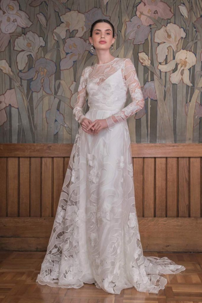 In questa foto una modella indossa un abito da sposa con sottoveste in cady e strato di tulle ricamato con la tecnica dell'intaglio. L'abito presenta maniche lunghe e corpetto girocollo