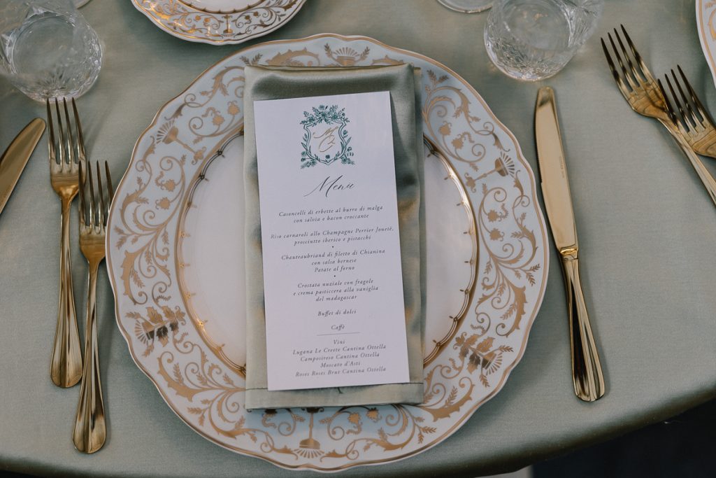 In questa foto la mise en place delle nozze di Mariavittoria e Claudio: piatti verde salvie e oro, posate dorate e menu che riprende la wedding stationery