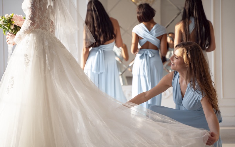 In questa foto una damigella della sposa che indossa un abito di colore turchese e piega in basso e le sistema lo strascico del vestito. Dietro di loro ci sono altre tre damigelle